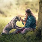 Hund und Halterin sitzen unter einem Baum und sind sich zugewandt